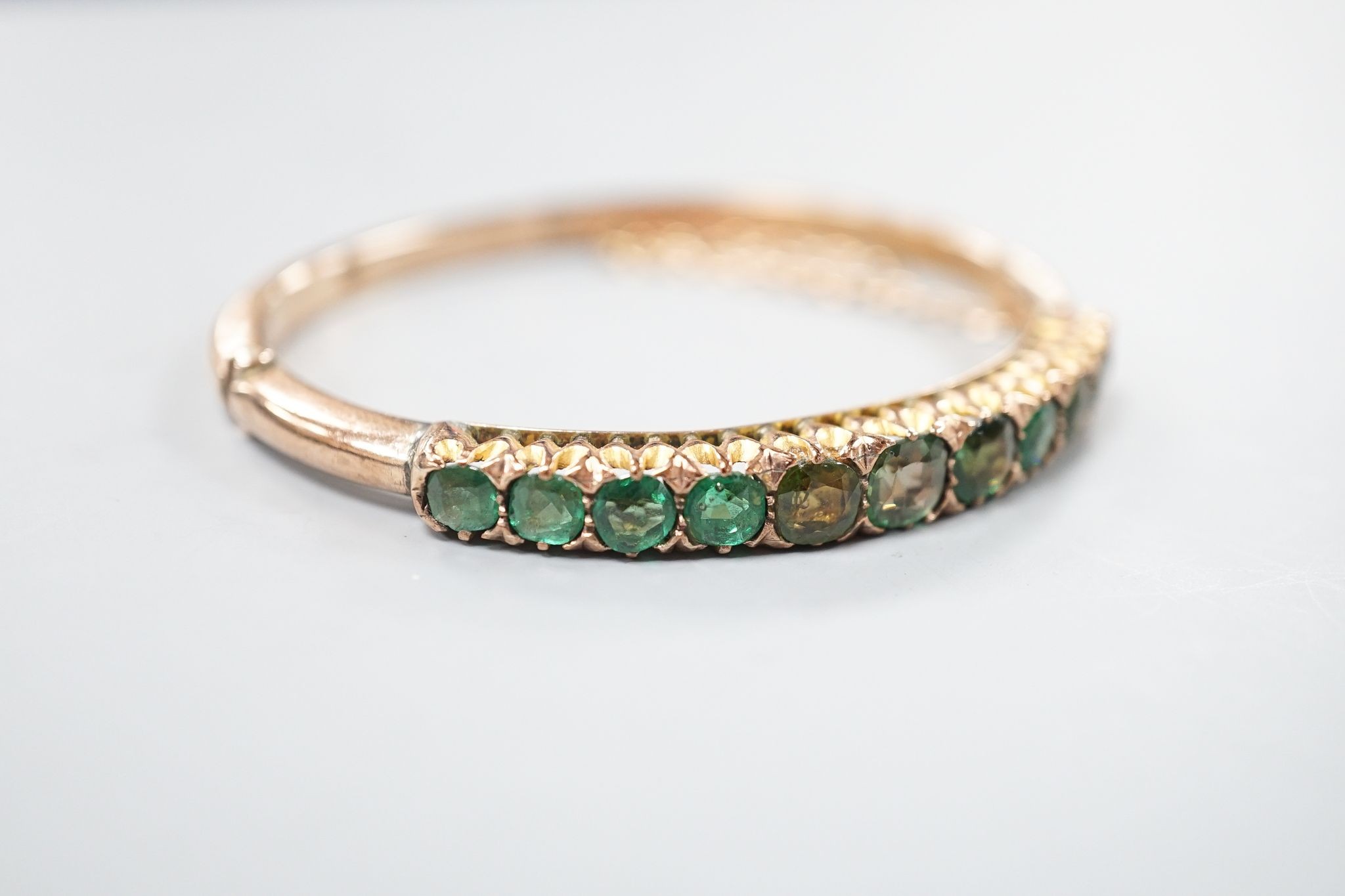 An Edwardian 9ct and graduated eleven green stone doublet set hinged bracelet, interior diameter 56mm, gross 12.6 grams.